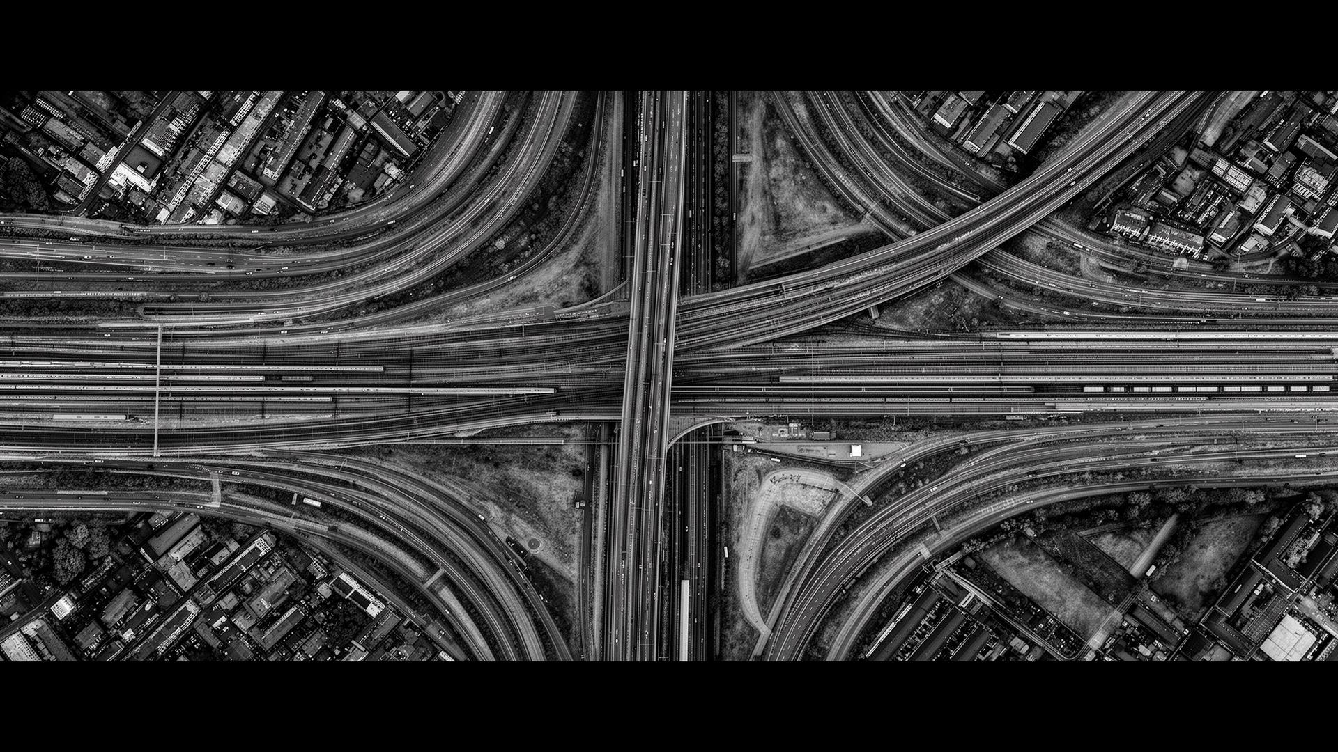 Aerial monochrome view of a transport interchange where many routes converge into a coherent system.